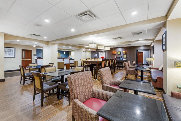 A hotel lobby with multiple seating areas, including tables and chairs, and a reception desk.