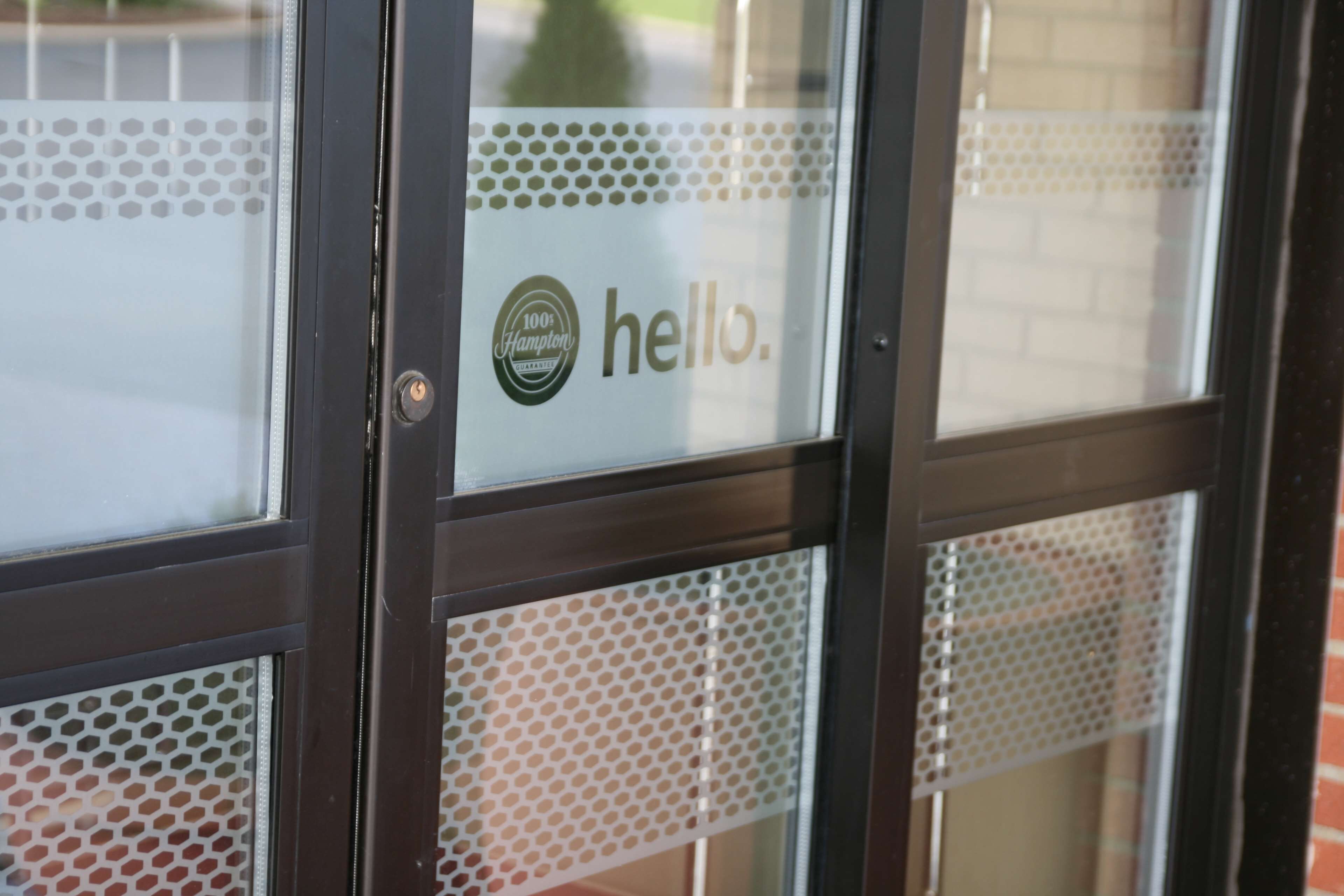 A glass door with a "hello." sticker and a Hampton Inn logo.