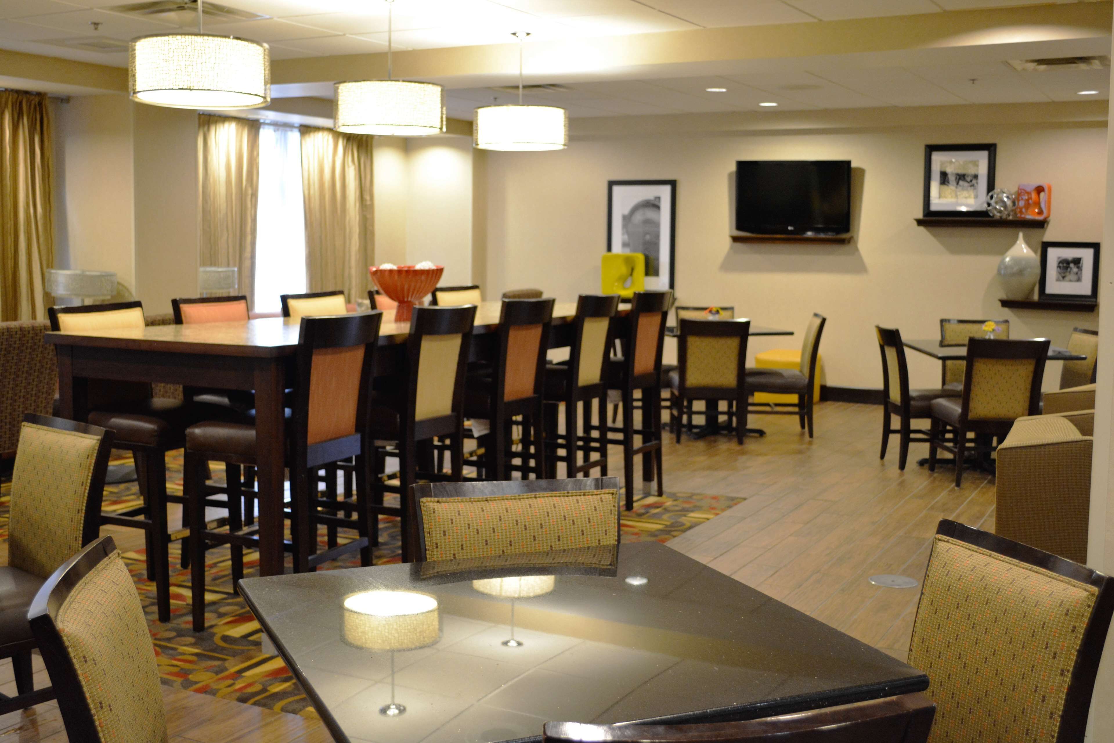 A hotel dining area with multiple tables and chairs, a television on the wall, and a patterned carpet.