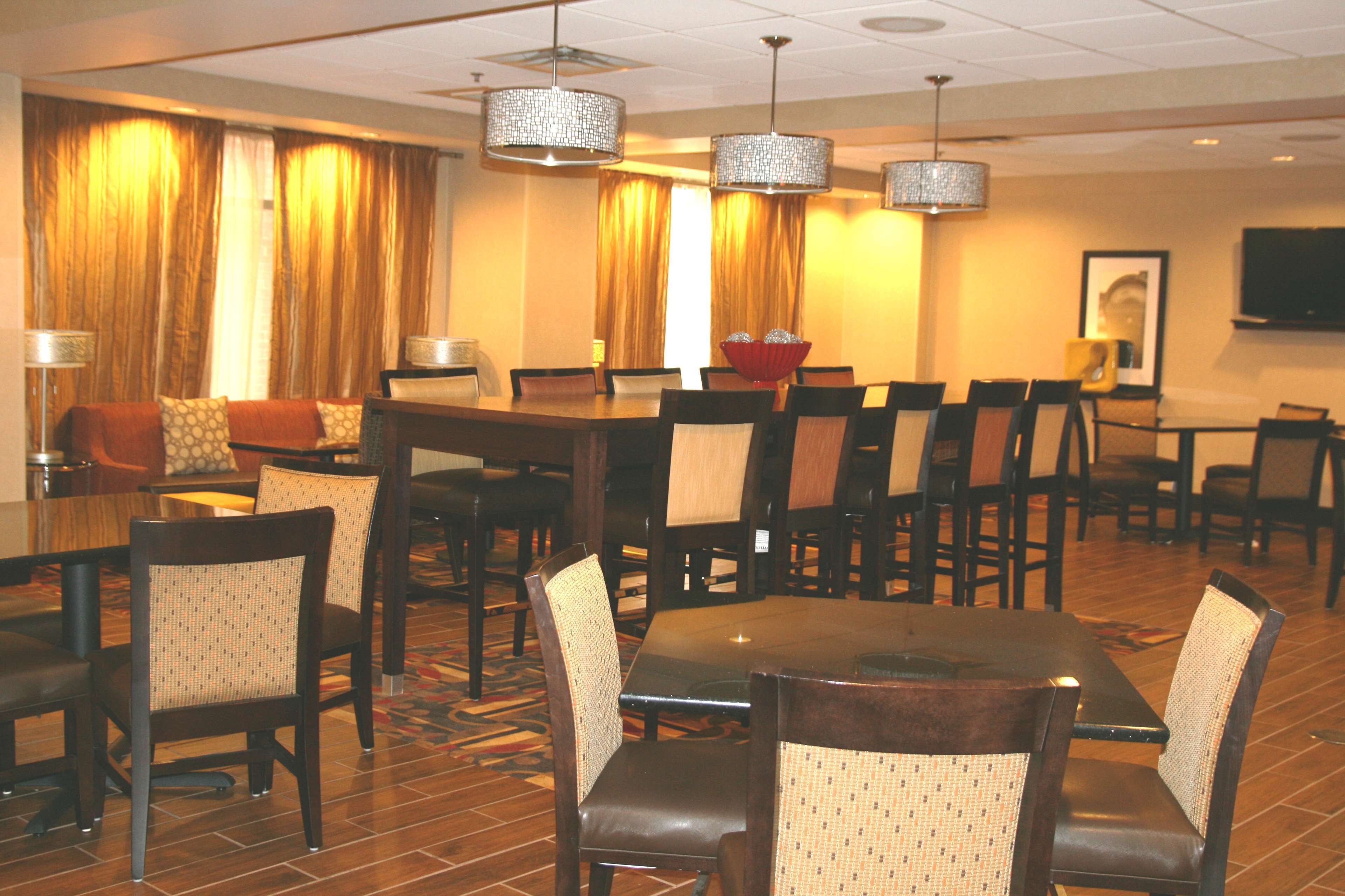 Une salle à manger d’hôtel avec plusieurs tables et chaises, un lustre et un téléviseur fixé au mur.