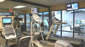 Un gimnasio con cintas de correr, bicicletas estáticas y un televisor que muestra un noticiero.