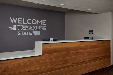 A reception desk with a grey wall behind it displaying "WELCOME TO THE TREASURE STATE" and a wooden panel design.