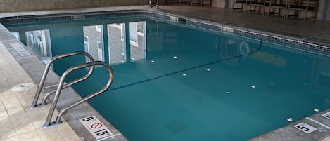 An indoor swimming pool with clear water, tiled floor, and a blue ceiling.