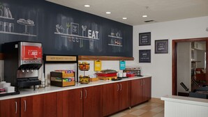A breakfast bar with a coffee machine, egg and juice dispensers, and a chalkboard menu.