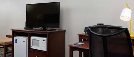Ein Hotelzimmer mit Flachbildfernseher auf Holzfuß, einer Mikrowelle, einem Kühlschrank, einem Schreibtisch mit Stuhl und einer Stehlampe.