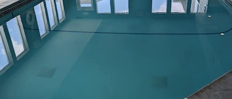 Una piscina interior con agua cristalina, paredes de azulejos y ventanas que ofrecen vistas al exterior.