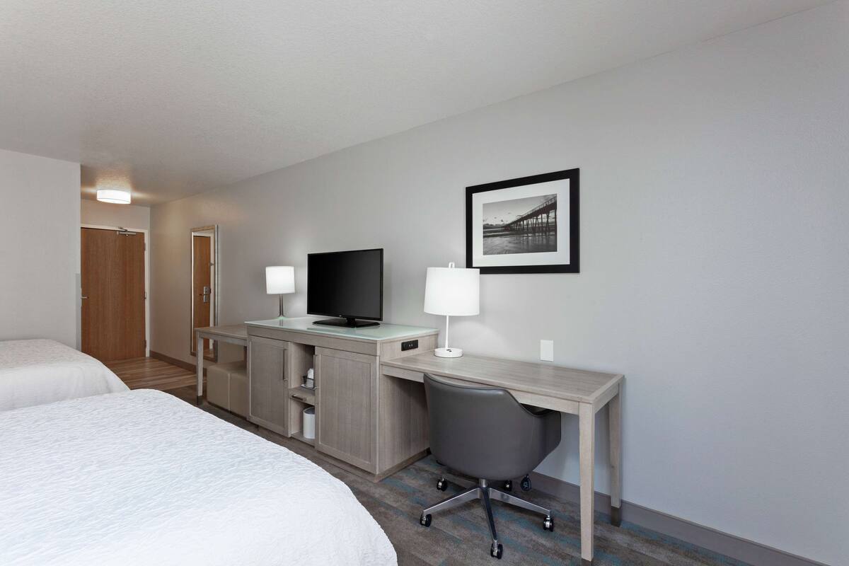 A hotel room with two beds, a desk with a computer, a TV, and a chair.