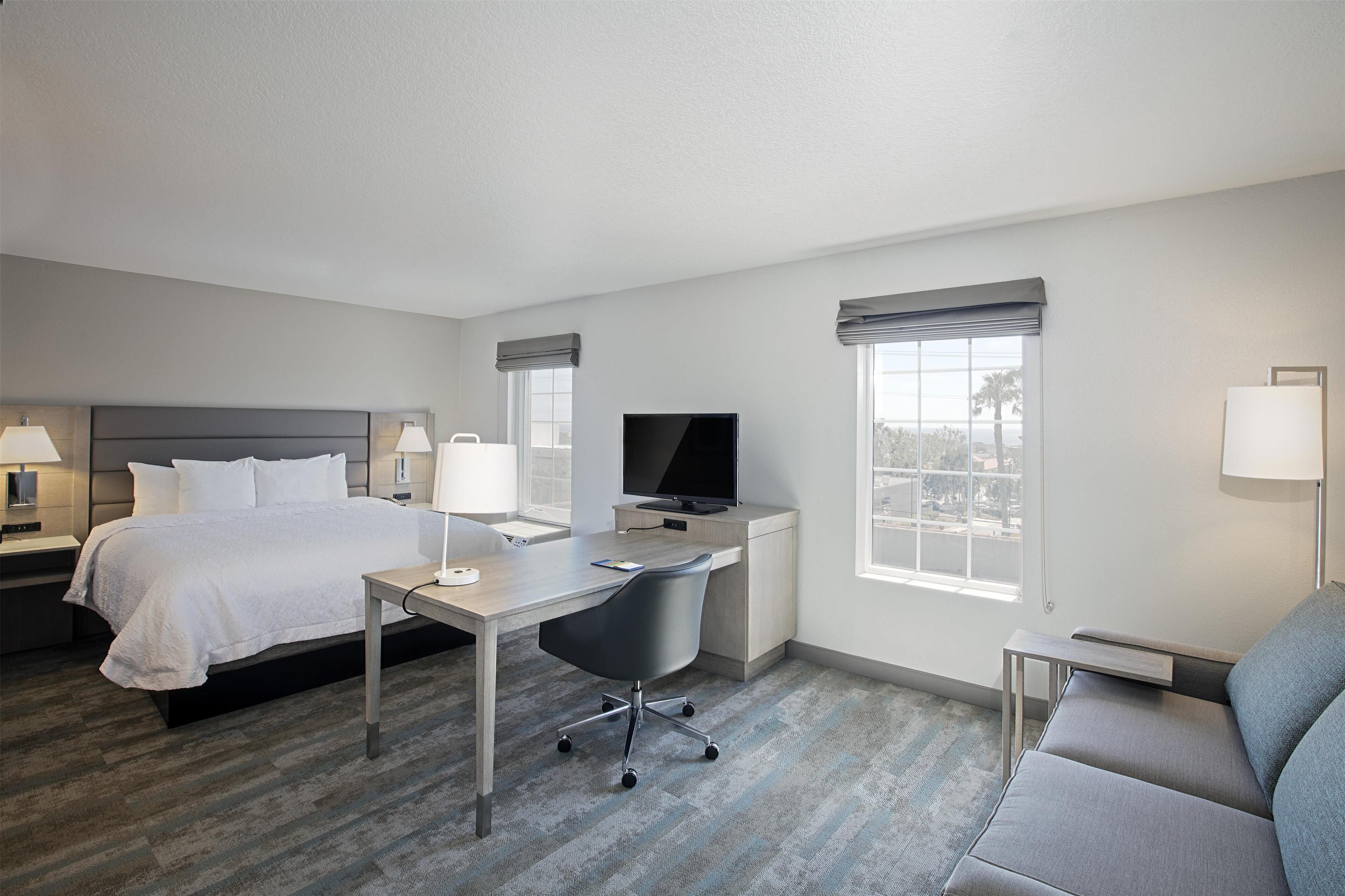 A hotel room with a bed, desk, TV, and a sofa.