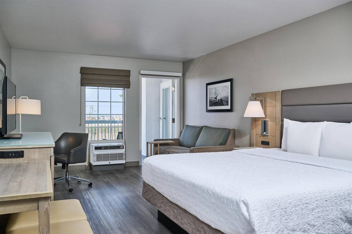 A hotel room with a bed, desk, chair, and a window with a view.