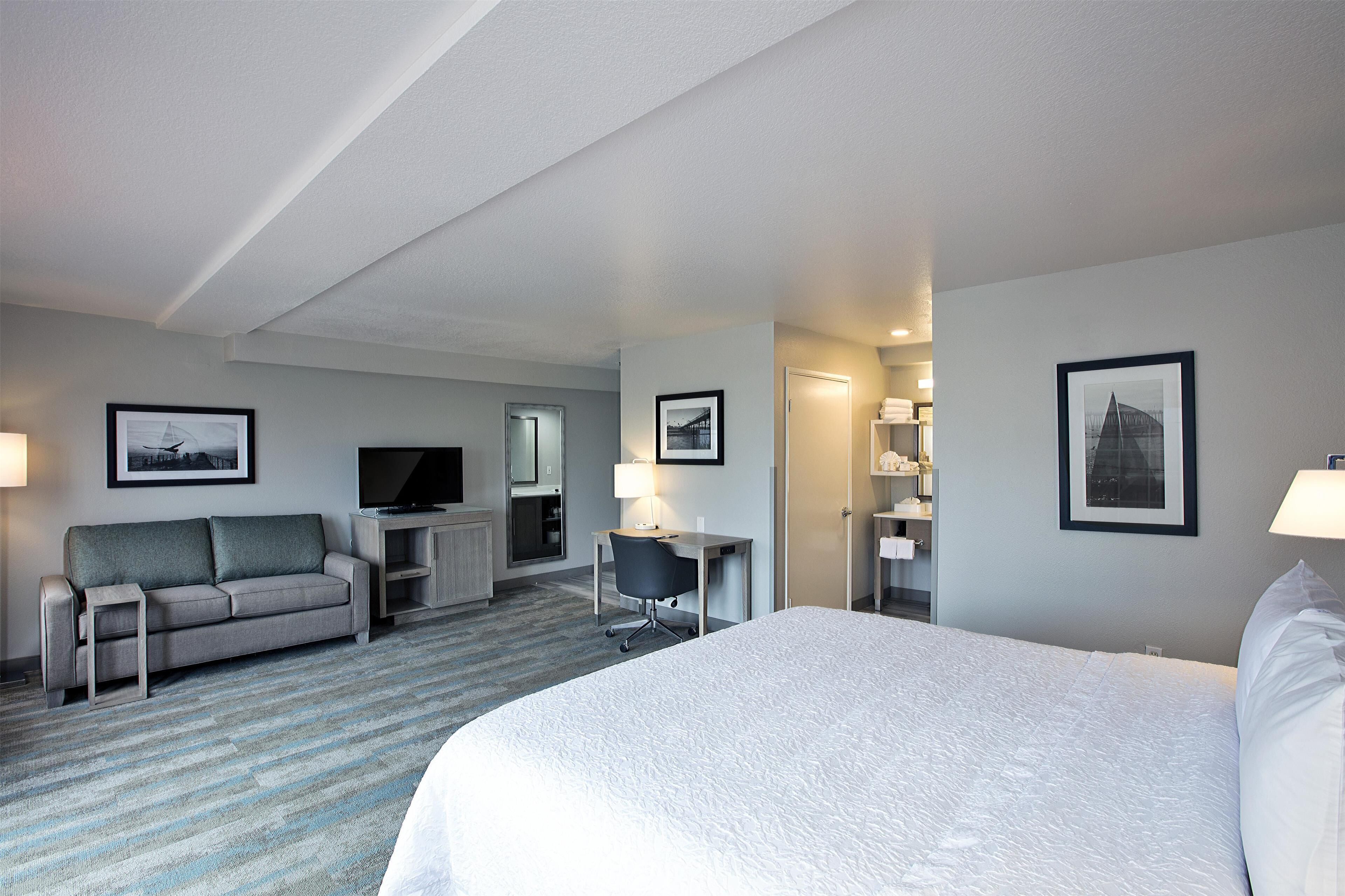 A hotel room with a large bed, a sofa, a desk, and a TV.