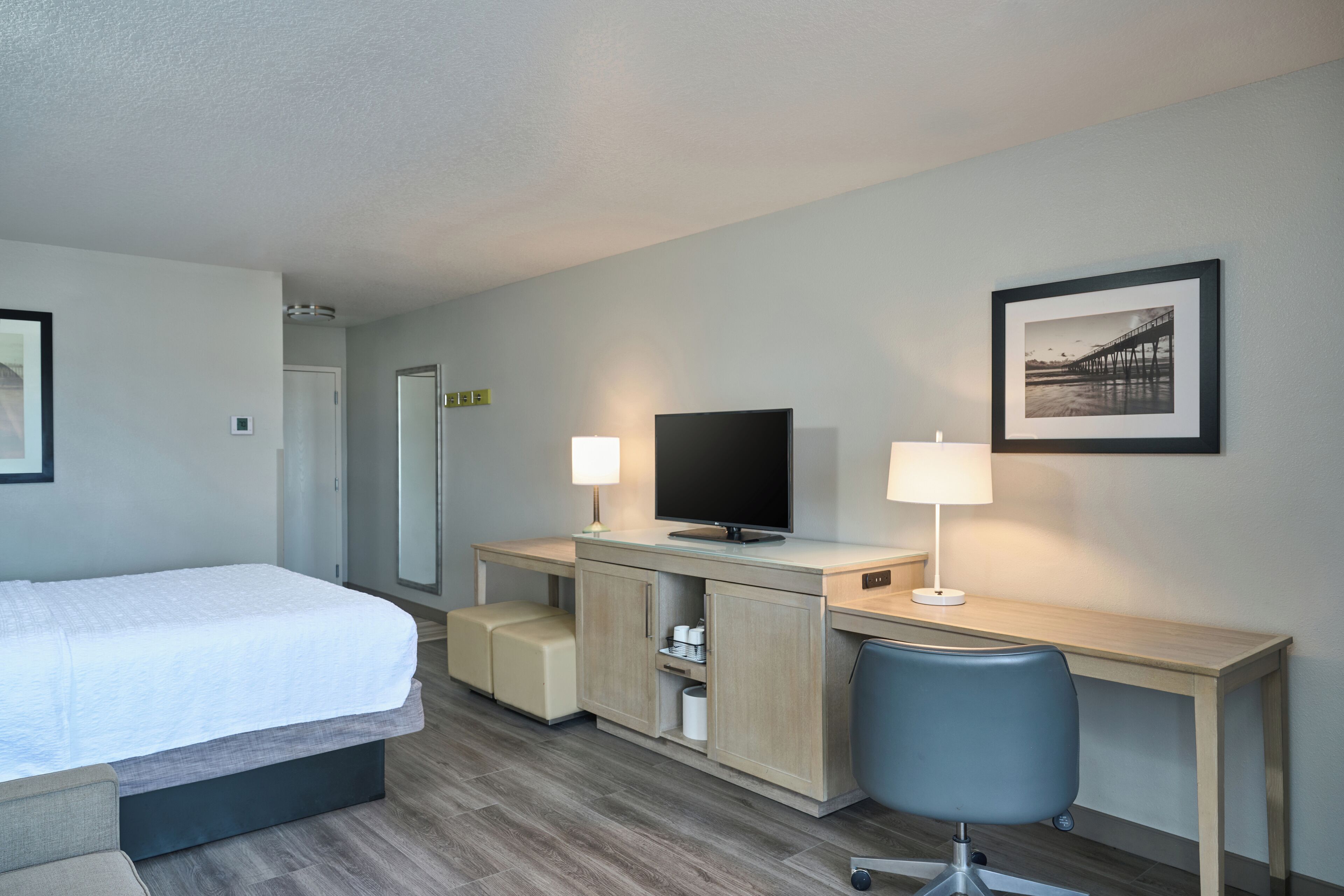 Una habitación de hotel con cama, escritorio, silla, televisor y un cuadro en la pared.