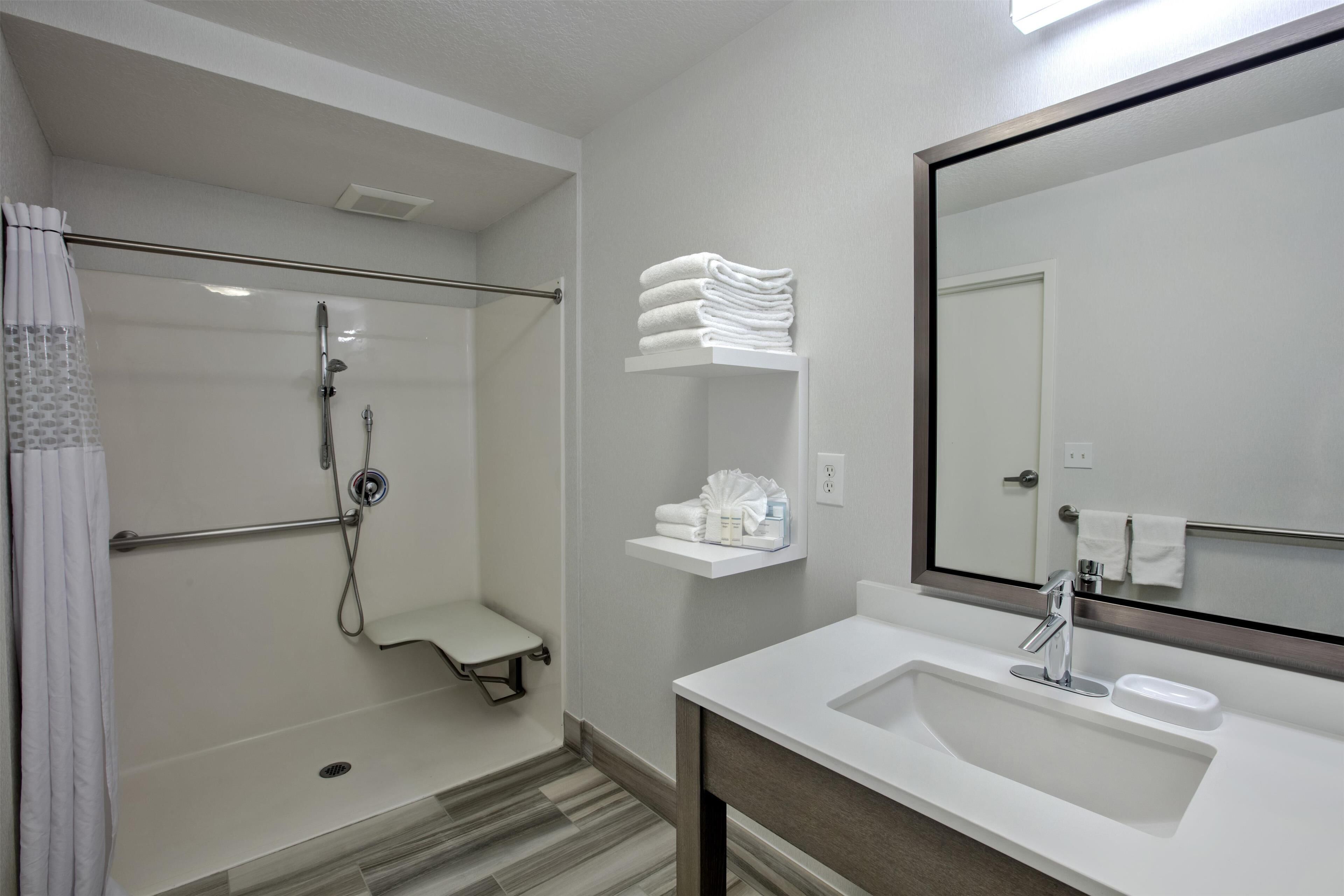 A modern bathroom with a walk-in shower, a sink with a mirror, and neatly stacked towels on a shelf.