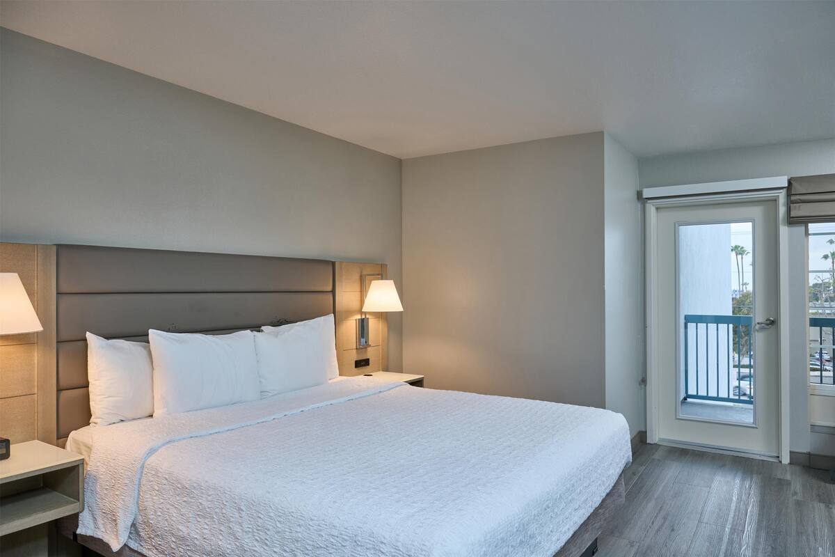 A hotel room with a large bed, two bedside lamps, a nightstand, and a door leading to a balcony.