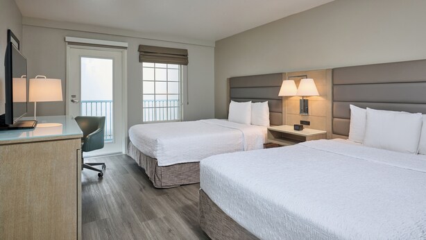 A hotel room with two beds, a desk, a chair, and a TV.