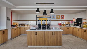 A modern kitchen with wooden cabinets, a central island with coffee makers, and a breakfast sign.