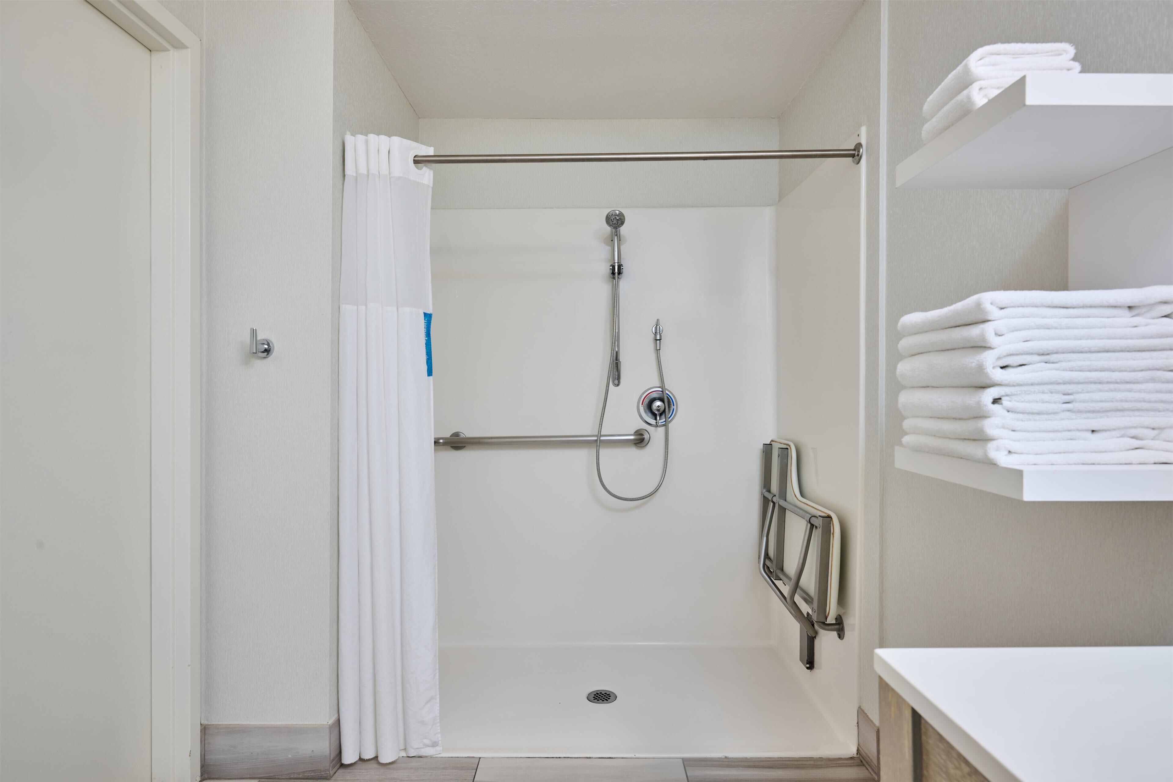 A walk-in shower with a showerhead, a grab bar, and a towel rack with folded towels.