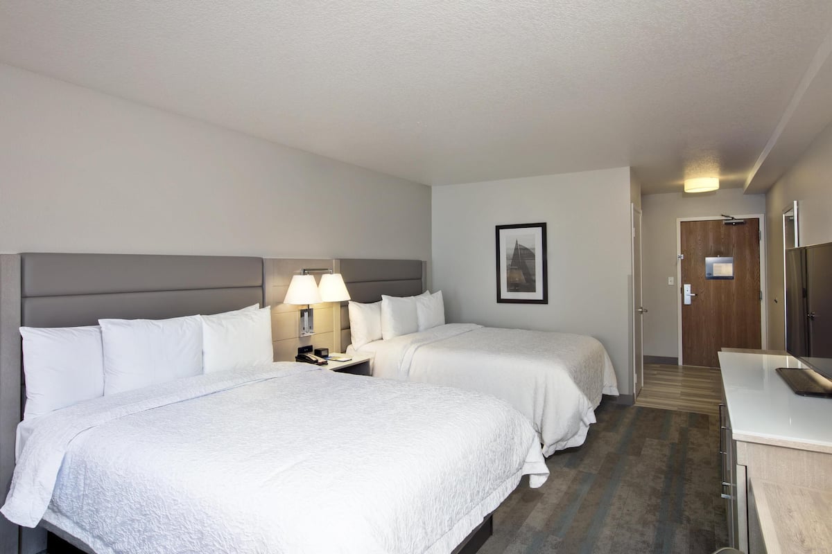 A hotel room with two beds, a nightstand with a lamp, a framed picture on the wall, and a door leading to another room.