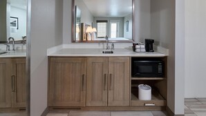 A modern bathroom with a large mirror, wooden cabinets, a sink, a coffee maker, and a microwave.