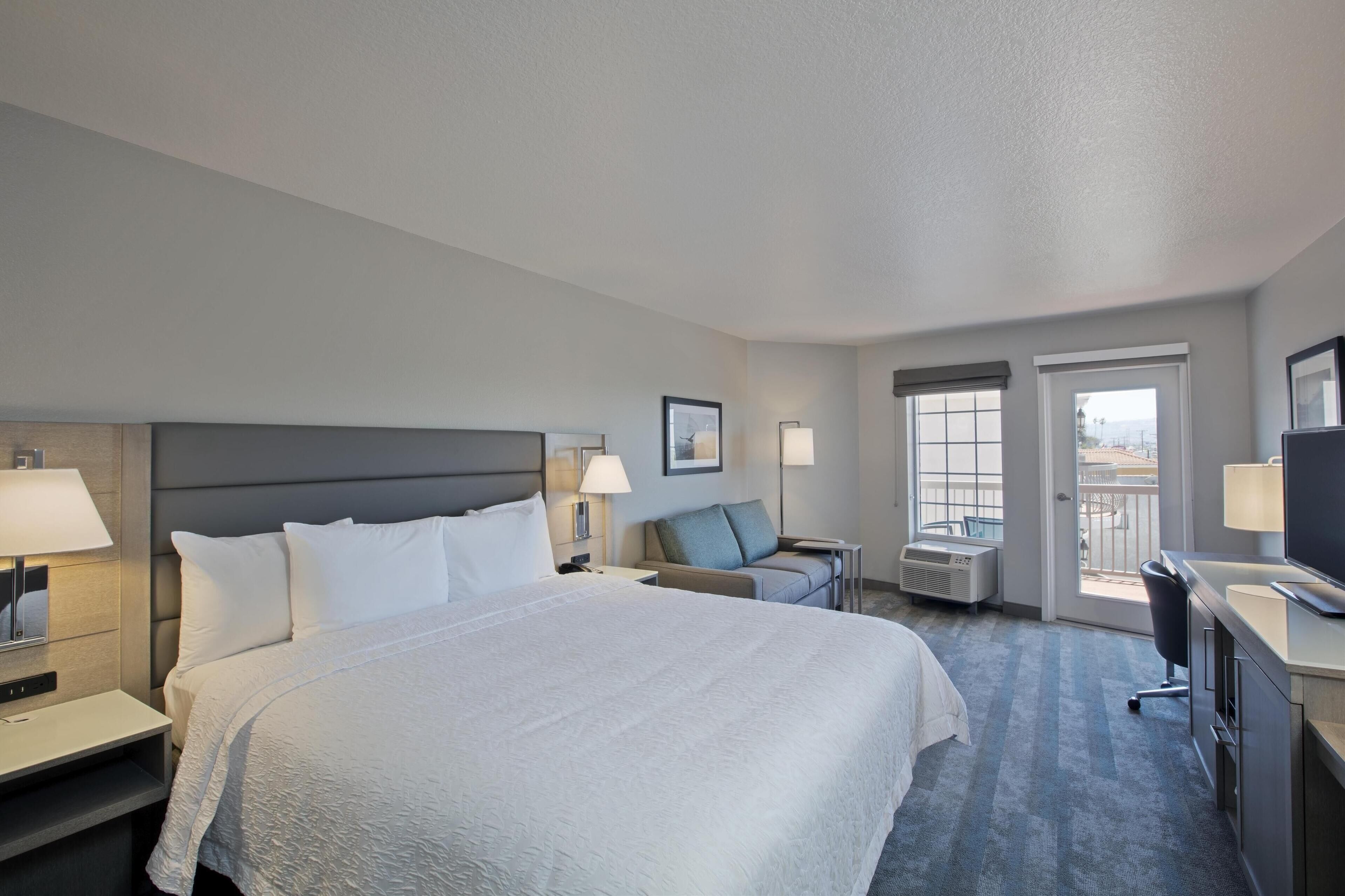 Une chambre d’hôtel avec un grand lit, un bureau, une chaise, une télévision et un balcon avec vue.