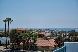 A Wells Fargo building with a red-tiled roof, surrounded by palm trees and other buildings, overlooking a coastal town.