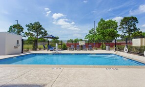 A rectangular swimming pool with a 3-foot depth marker, surrounded by a black fence, with lounge chairs and umbrellas. - Hampton Inn Houston-Pearland (Pearland)