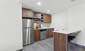 A modern kitchen with stainless steel appliances, wooden cabinets, and a bar stool. - Hampton Inn Houston-Pearland (Pearland)