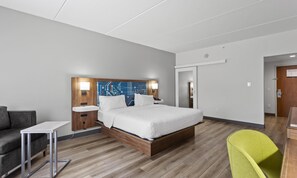 A modern hotel room with a wooden bed, bedside tables, a grey sofa, and a bright green chair. - Hampton Inn Houston-Pearland (Pearland)