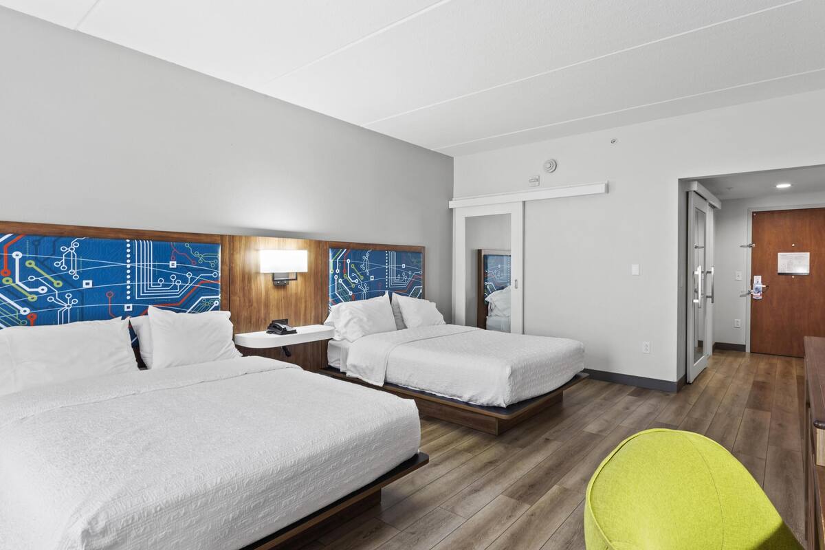 A hotel room with two beds, a desk, a chair, and a door.
