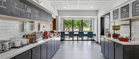A modern kitchen with a central island, a chalkboard wall with food-related drawings, and a view of the outdoors through large windows.