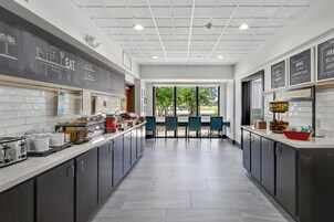 Cozinha moderna com ilha central, parede de lousa com desenhos de comida e vista para o exterior por grandes janelas.