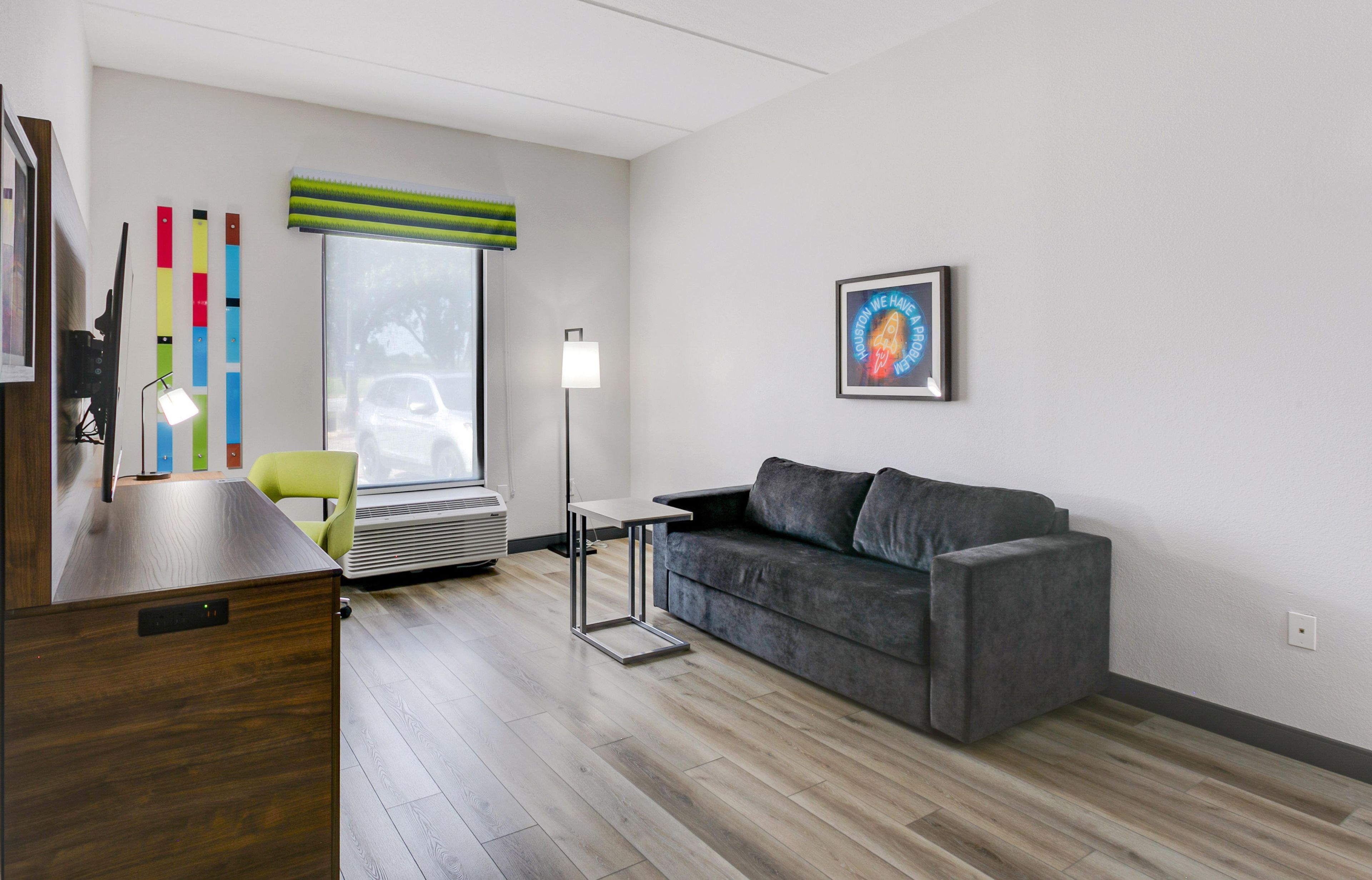 A modern living room with a grey sofa, a small table, a floor lamp, and a window with blinds.