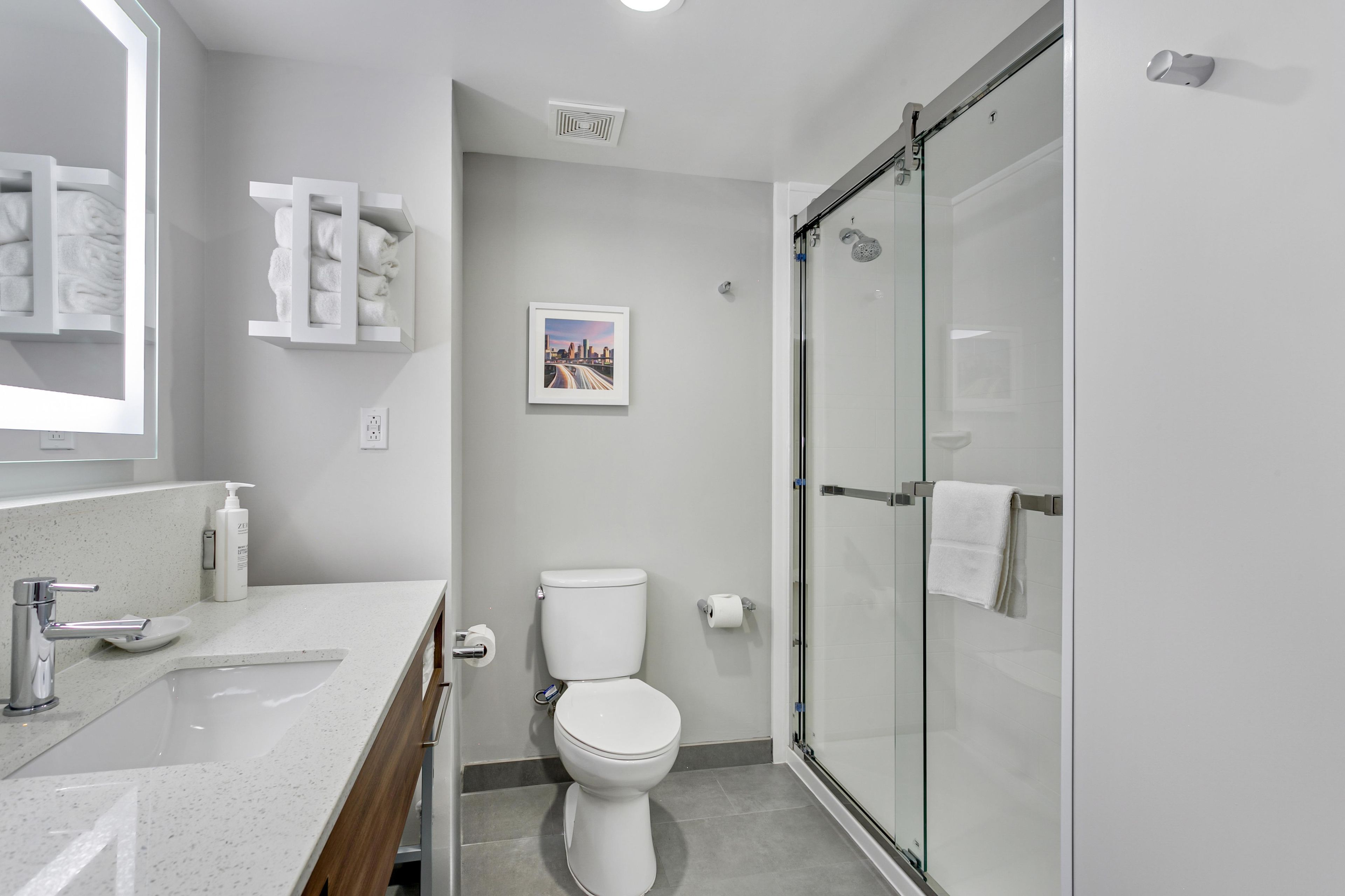 Un baño moderno con cabina de ducha de vidrio, inodoro blanco y lavabo con espejo sobre él.