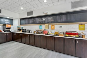 A modern kitchen with a chalkboard menu, a coffee machine, and various breakfast items. - Hampton Inn Houston-Pearland (Pearland)