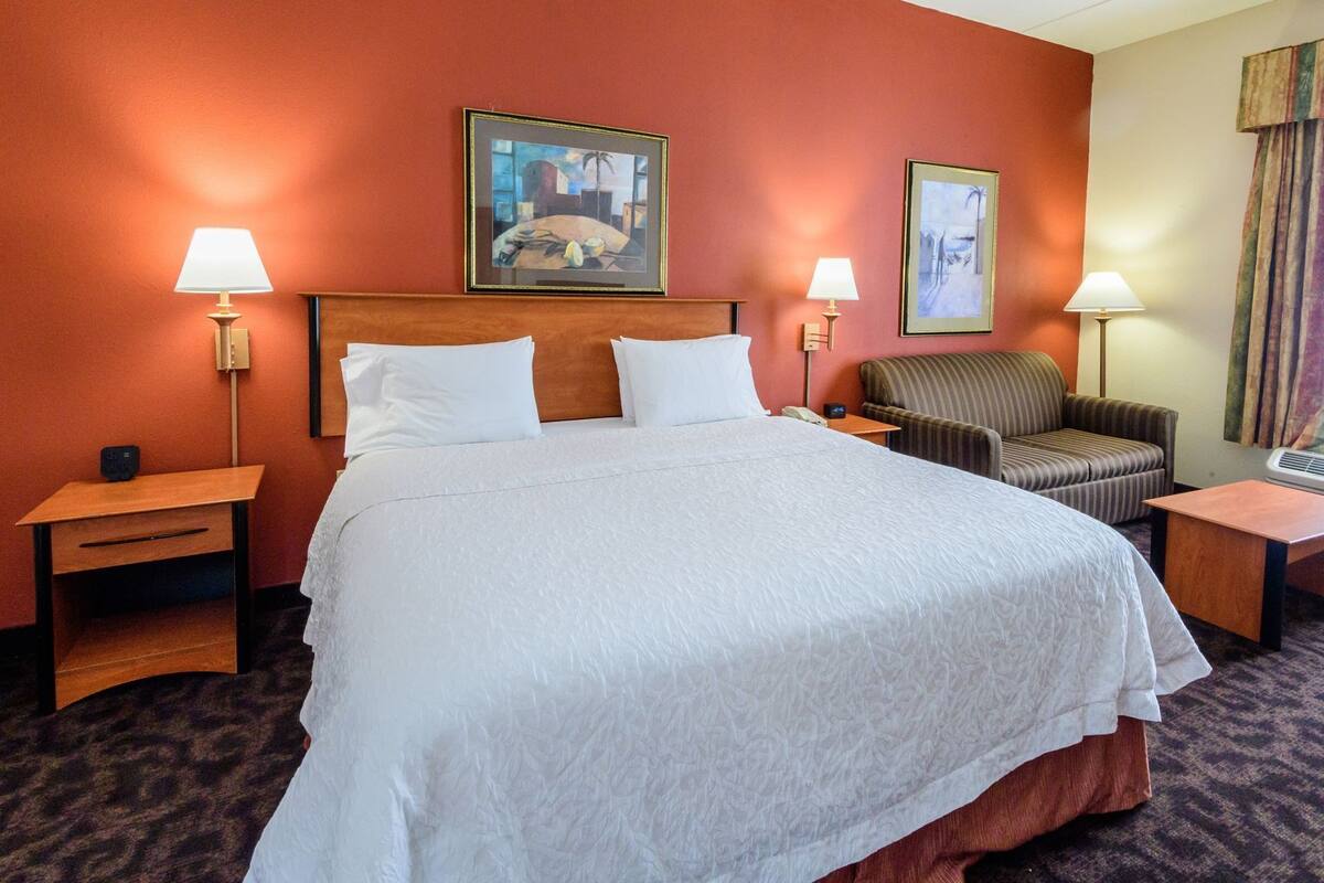 A hotel room with a large bed, two bedside tables, a chair, and two wall-mounted lamps.