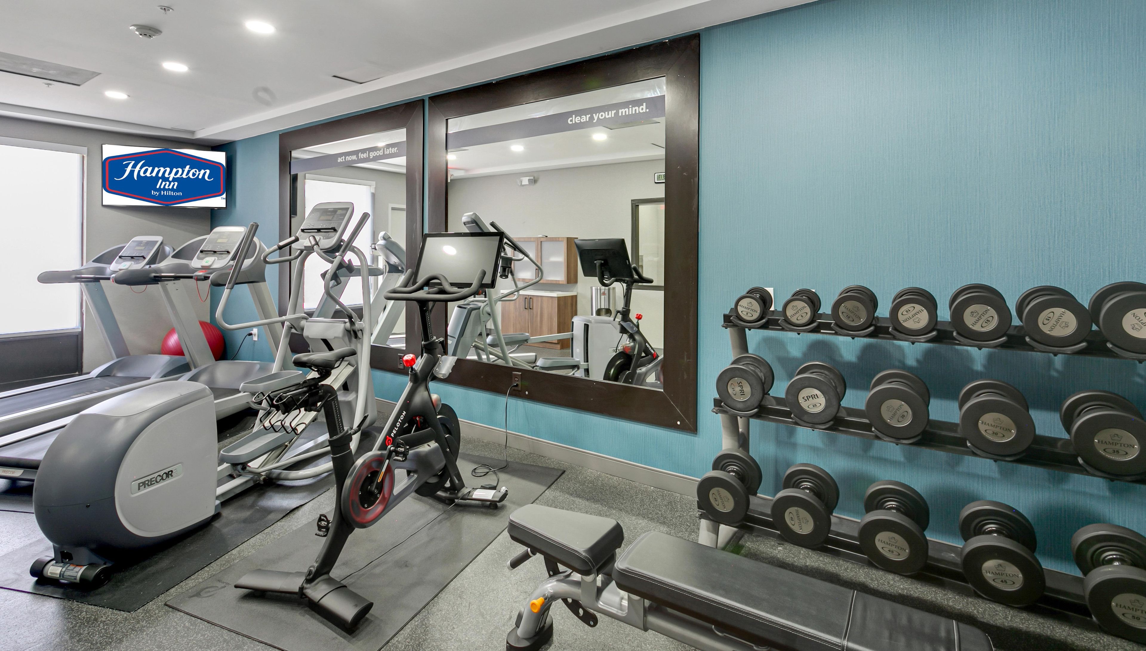 Een sportschool met loopbanden, een crosstrainer, een hometrainer en een rek met gewichten.