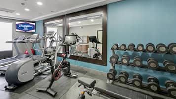 Een sportschool met loopbanden, een crosstrainer, een hometrainer en een rek met gewichten.