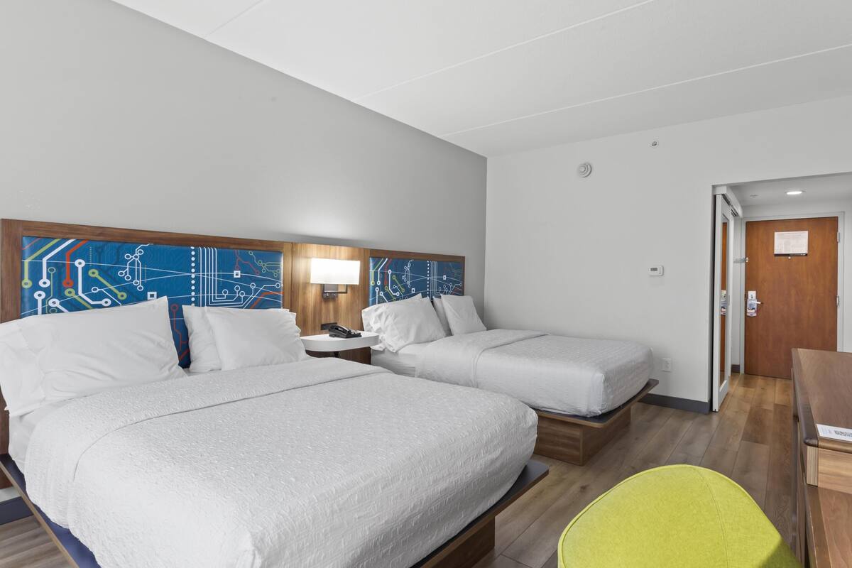 A hotel room with two beds, a desk, a chair, and a wall with a circuit board design.