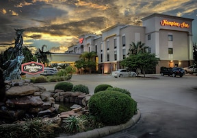 Un hotel Hampton Inn con estacionamiento, una estatua y un jardín ajardinado.