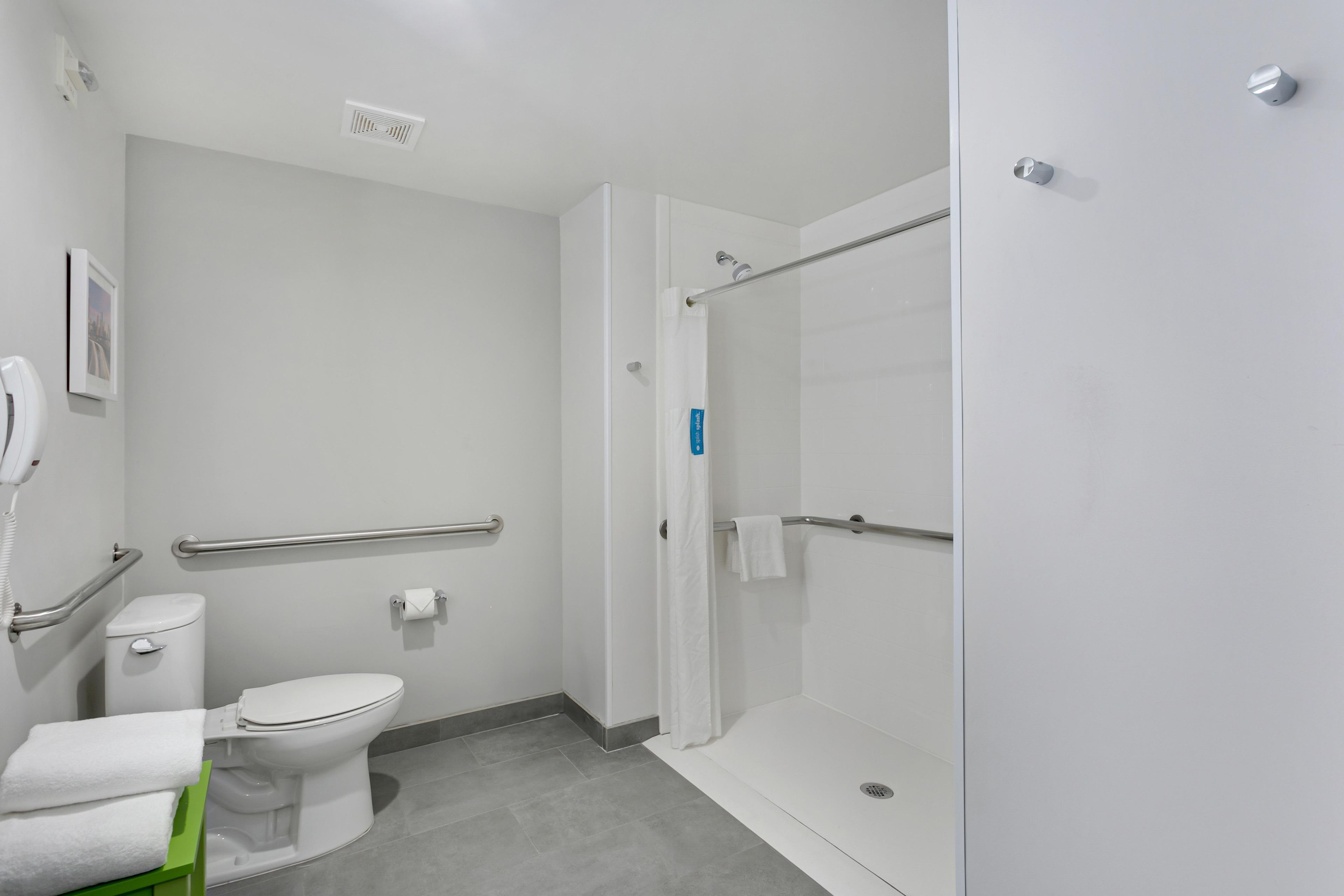 A modern bathroom with a toilet, a shower, and a handrail.