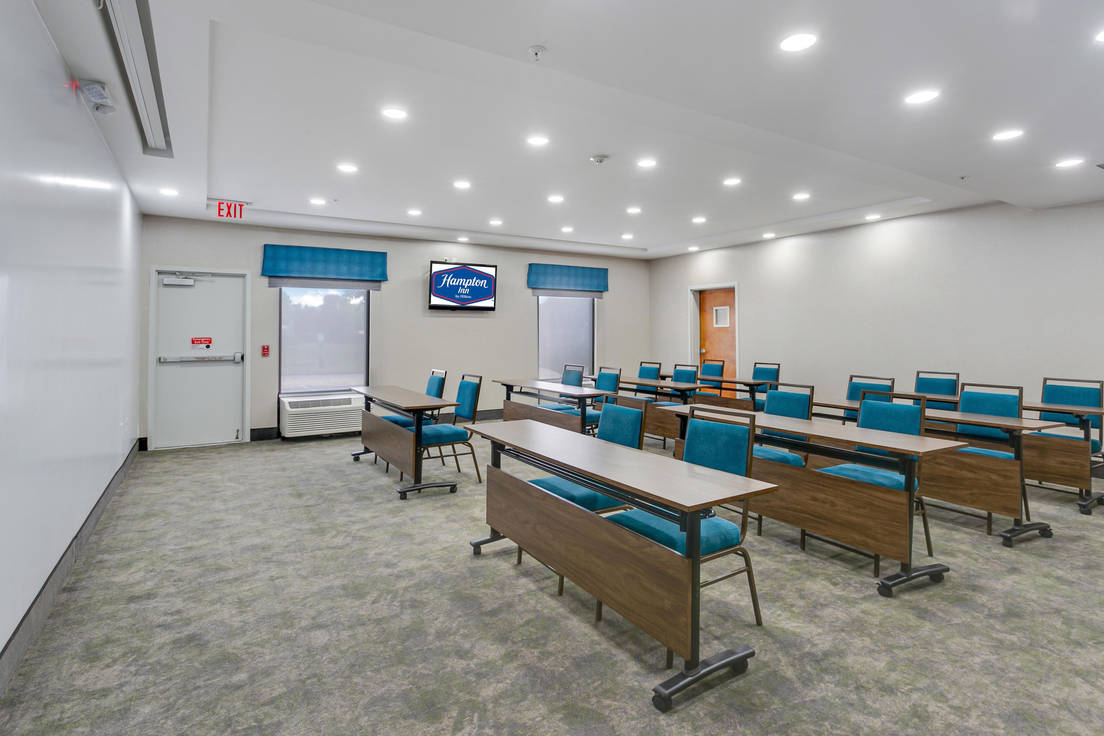 Una sala de conferències amb diverses taules i cadires, un senyal d'emergència i el distintiu d'Hampton Inn.