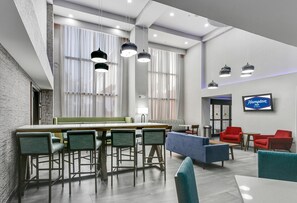A modern hotel lobby with a bar area, seating, and a television screen displaying the hotel name. - Hampton Inn Houston-Pearland (Pearland)