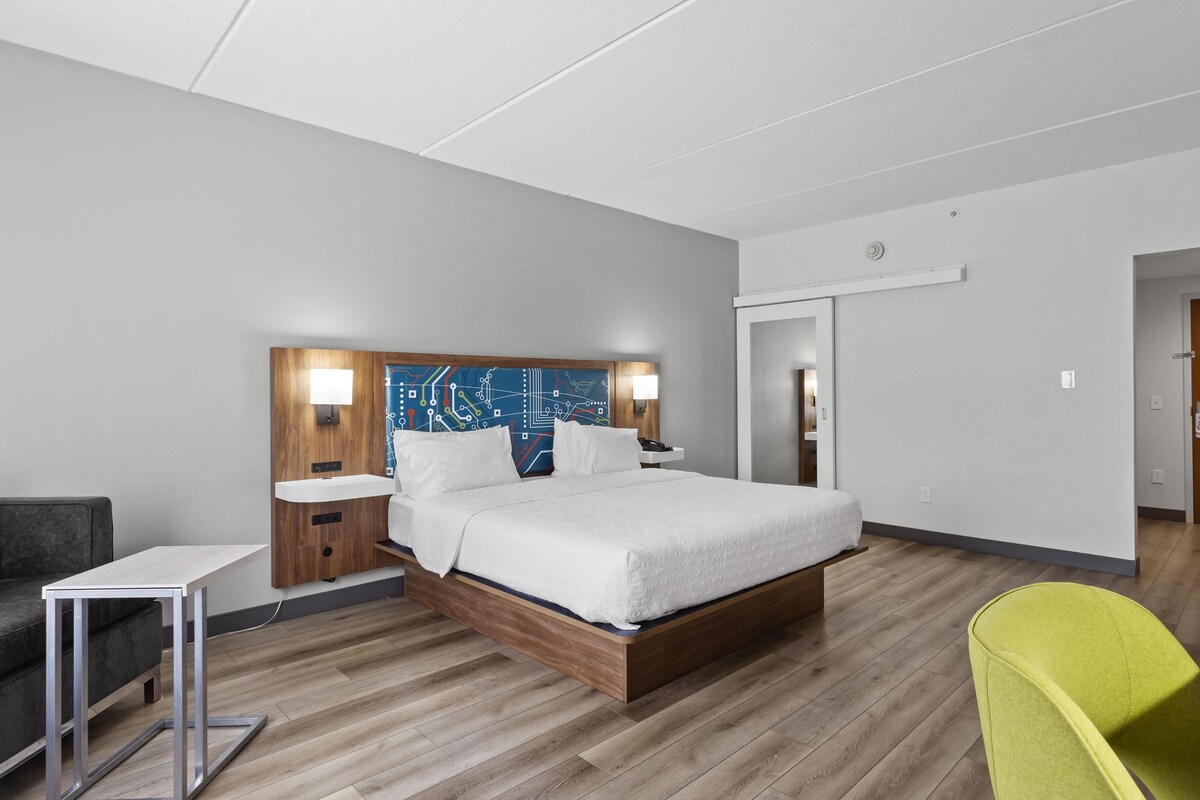 Et moderne hotelværelse med en træseng, sengeborde, en grå sofa og en lysgrøn stol.
