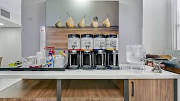 A coffee station with multiple coffee dispensers, a water dispenser, and a tray of cookies and pastries.
