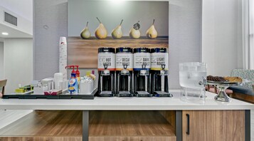 Una estación de café con varios dispensadores de café, un dispensador de agua y una bandeja de galletas y pasteles.