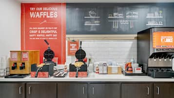 Een keukentrap met apparatuur voor het maken van wafels, een koffieapparaat en een sapdispenser.