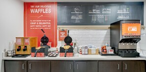 Una encimera de cocina con equipos para hacer gofres, una cafetera y un dispensador de jugo.