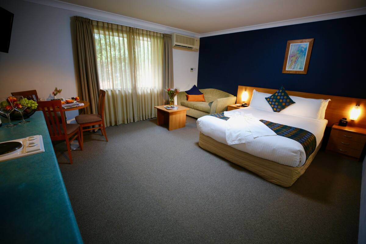 A hotel room with a bed, a desk, a chair, a sofa, and a dining table.