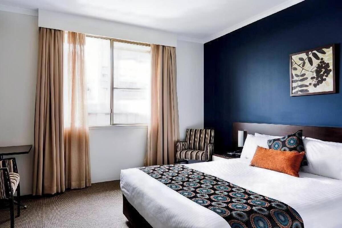 A hotel room with a large bed, a desk, a chair, and a window with curtains.