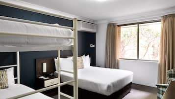A hotel room with bunk beds, a desk with a chair, a bedside table, and a window with curtains.