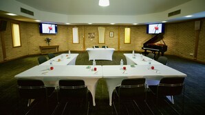 Une salle de conférence avec une longue table, des chaises, un piano et deux téléviseurs fixés aux murs.